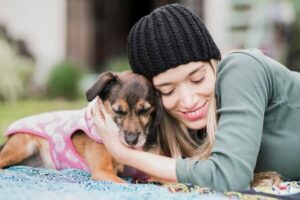 Smiling woman cuddling with her small dog on a blanket outdoors.